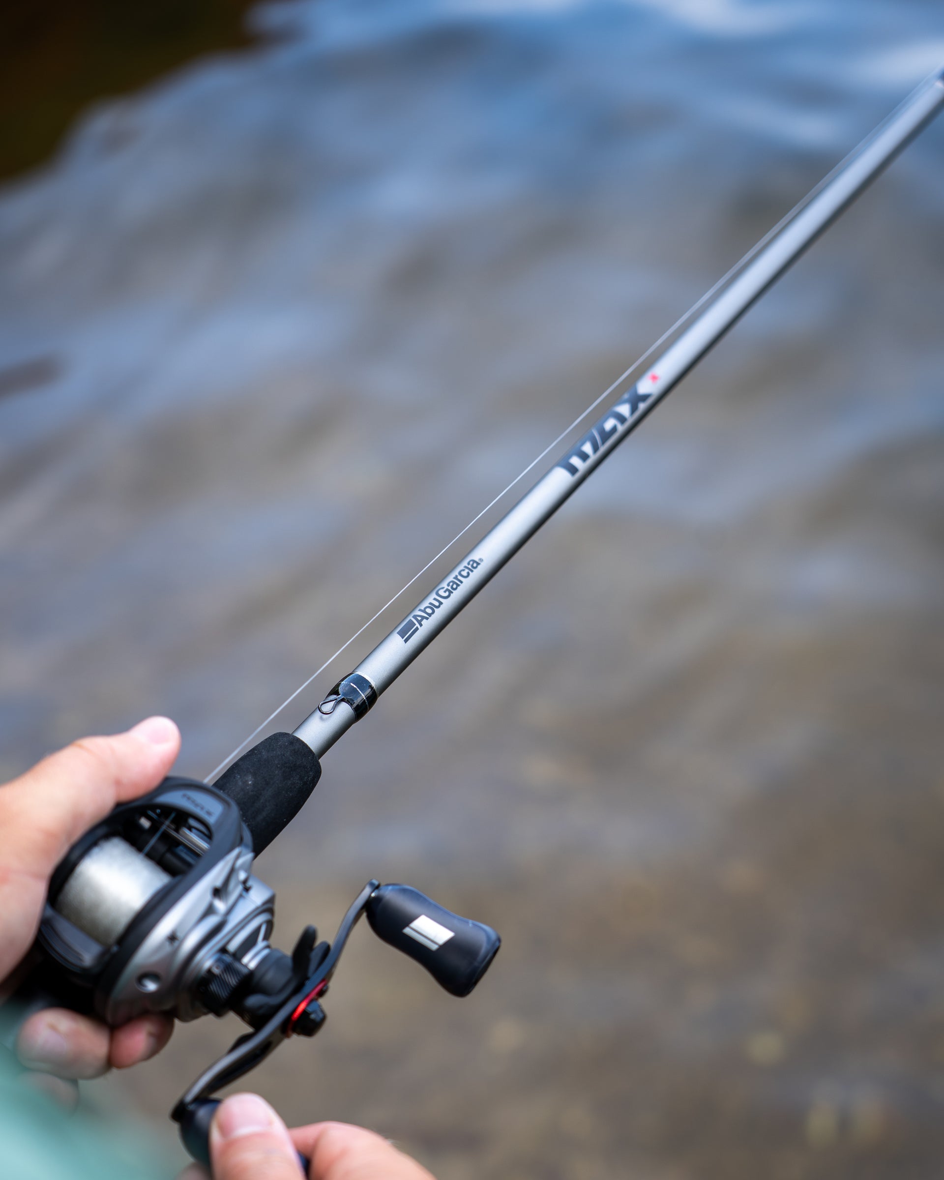 Abu Garcia Max X Low Profile Baitcast Combo in someone's hand reeling over water/. 