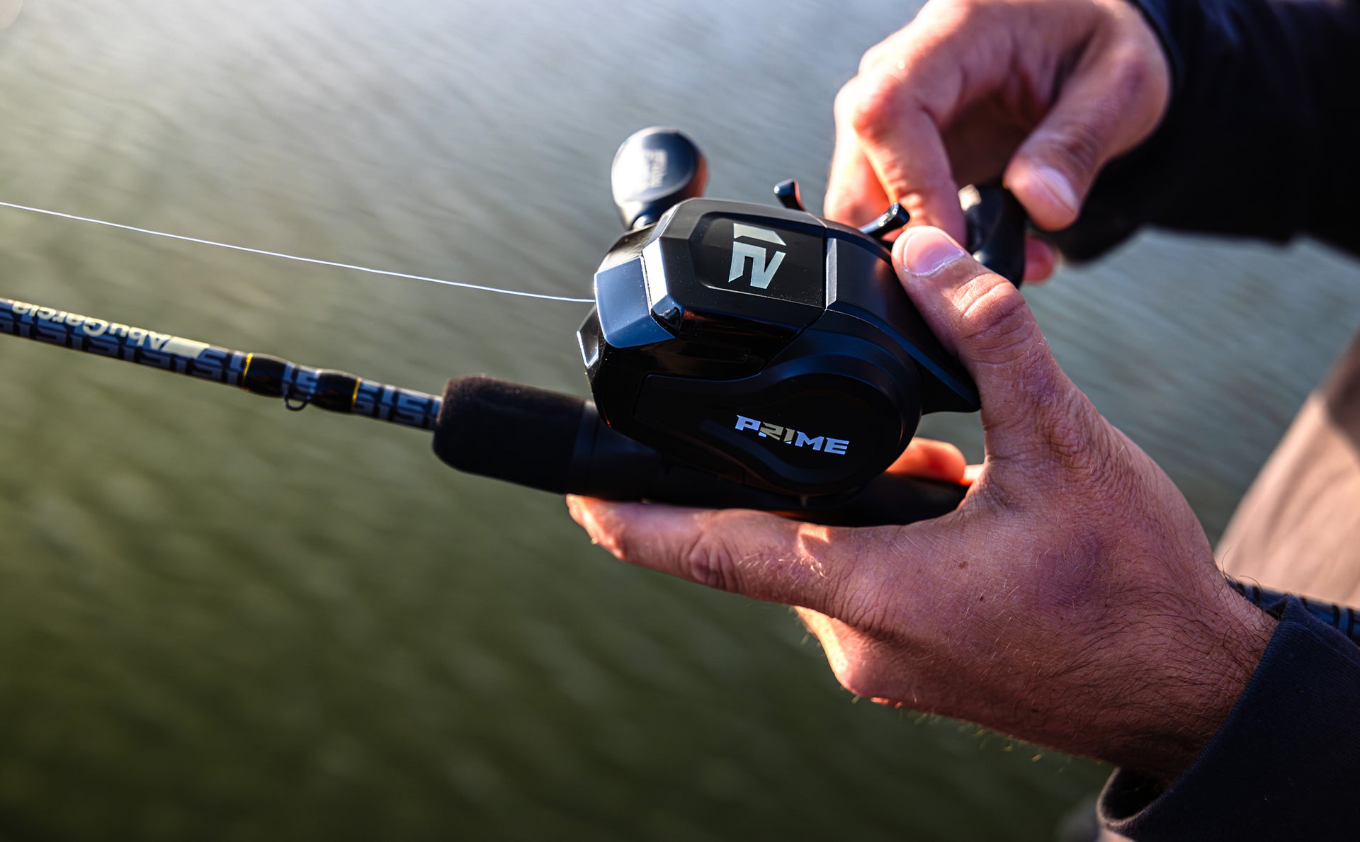 Fishing rod with a close-up of a person's hand holding the reel, with water in the background